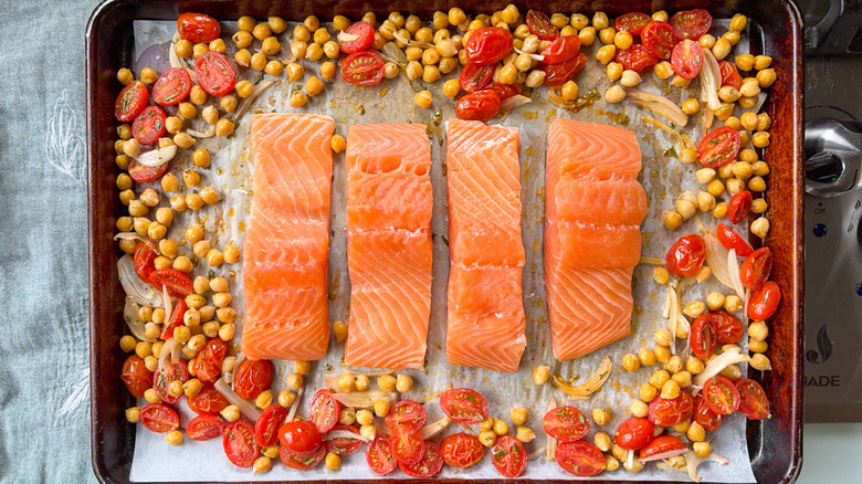 Raw salmon filets on baking sheet with chickpeas, grape tomaotes, and shallot