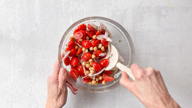 Stirring chickpeas, shallot, grape tomatoes, and rosemary in glass bowl with wooden spoon