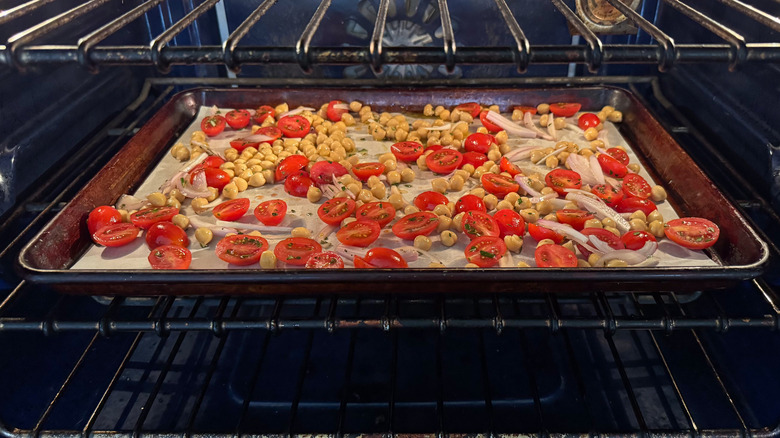 Chickpeas, grape tomatoes, and sliced shallot on parchment-lined baking sheet in oven