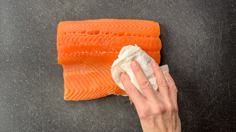 Patting salmon filet dry with paper towel on cutting board