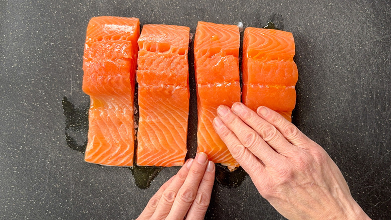 Rubbing olive oil into 4 salmon filets on cutting board