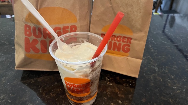 A Frozen Coke is mixed with vanilla soft serve in a cup with a spoon and a straw.