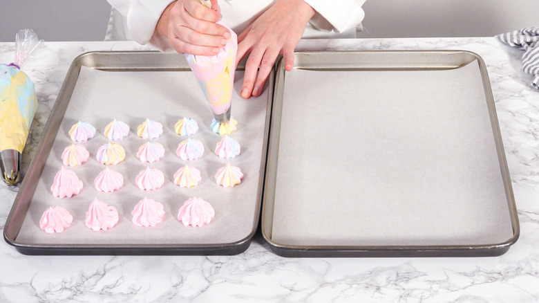 Piping multi-colored meringue cookies on baking sheets lined with parchment paper