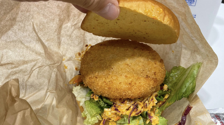 person opening shrimp katsu burger wrapped in brown paper