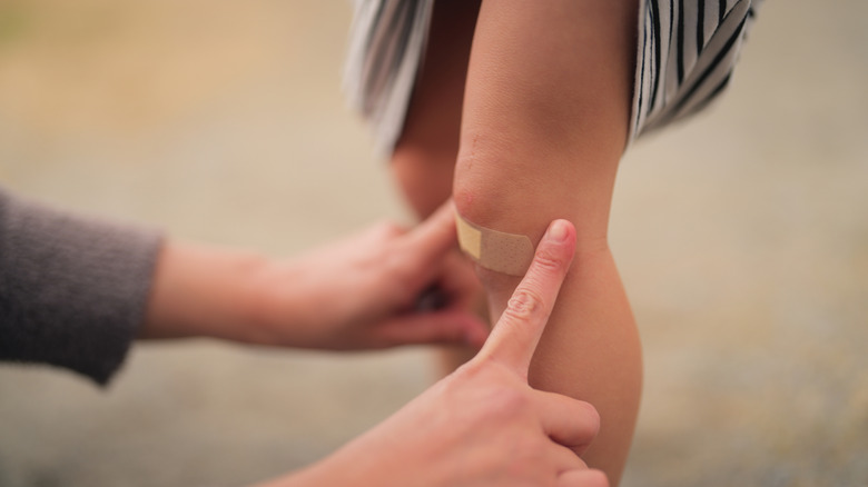 Woman's hands placing adhesive bandage on girl's knee