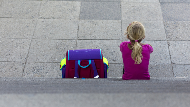 Back view of girl in pink shirt sitting on steps next to backpack