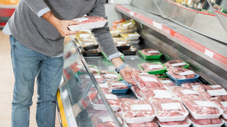 Hands picking out packages of meat at the grocery store