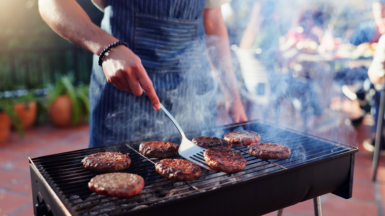 A person holding a spatula flipping a burger on a charcoal grill
