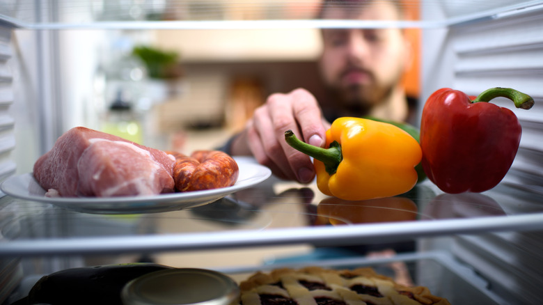 Raw meat and sausages stored on plate in fridge next to bell peppers
