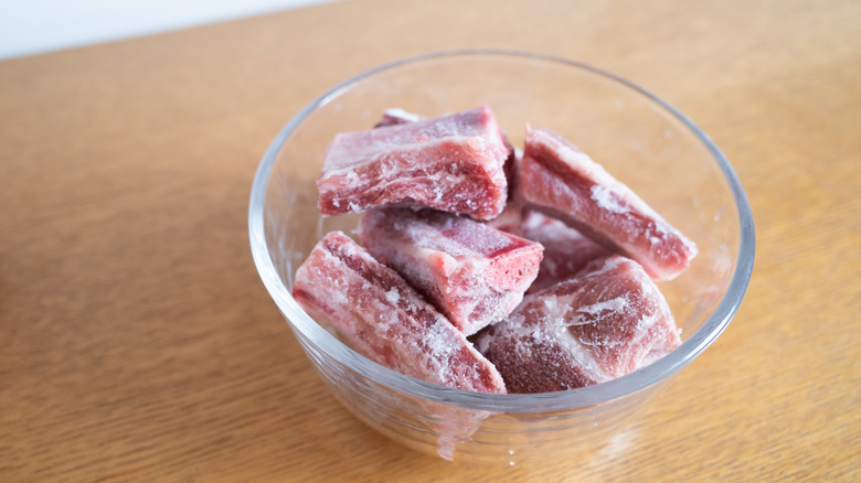 Frozen raw meat thawing in glass bowl on counter