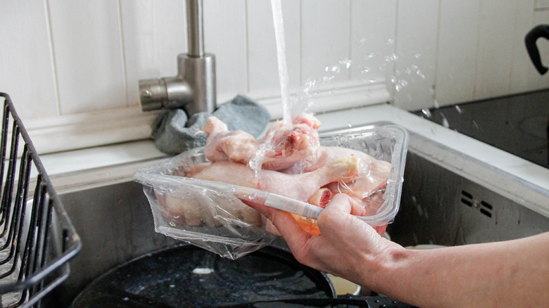 A container of chicken legs being rinsed in sink