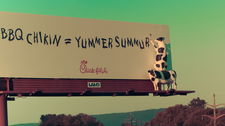 Two cows paint a message on a Chick-fil-A billboard.