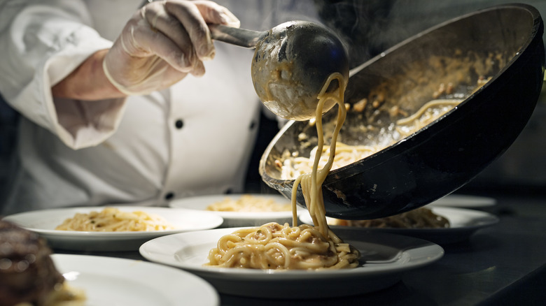 A chef ladling pasta on a plate