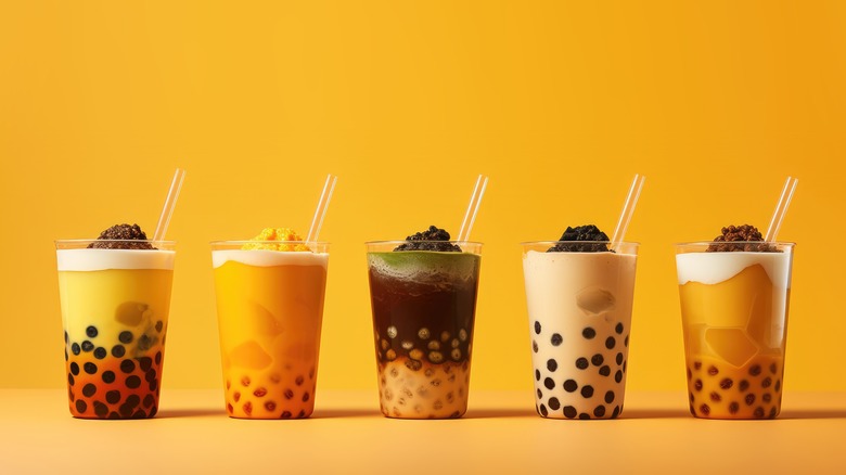 Five bubble tea drinks with straws, against an orange background