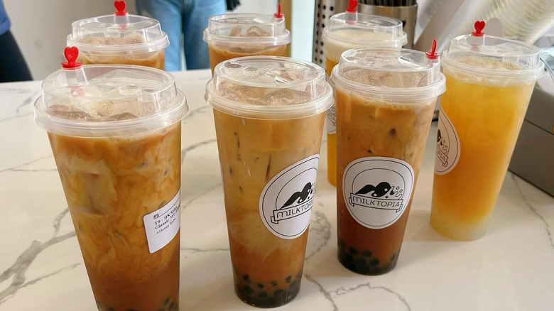 Seven Milktopia bubble tea cups on a white counter