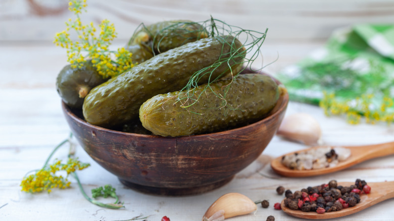 Bowl of dill pickles with peppercorns and garlic nearby