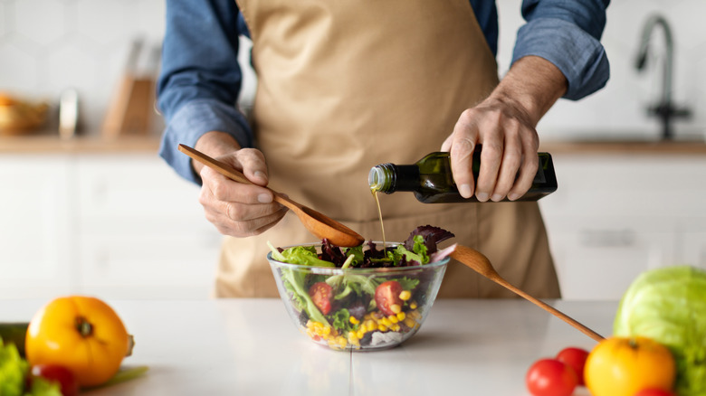 man drizzling oil on salad