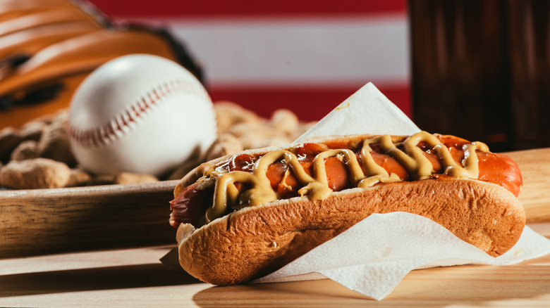 A hot dog in a bun with a baseball in the backdrop