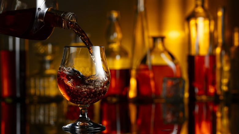 Brandy being poured in glass with bottles in background