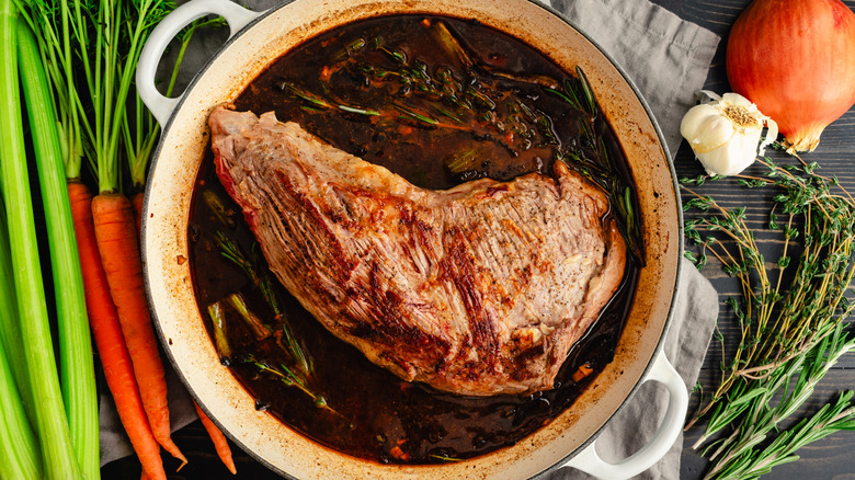 A steak in a cast iron Dutch oven with liquid, herbs, celery, carrots, and garlic