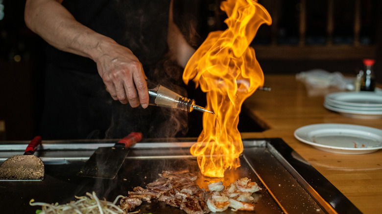 Chef cooks over an open flame on a griddle