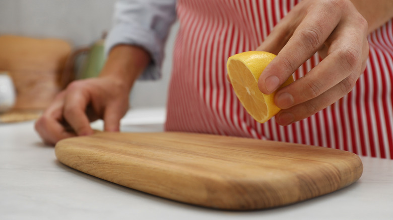 Person holding half a lemon above wooden cutting board