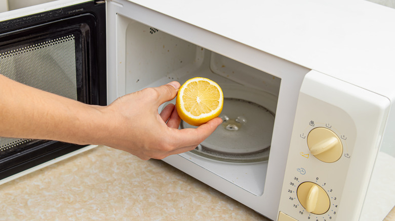 Person holding half a lemon near microwave