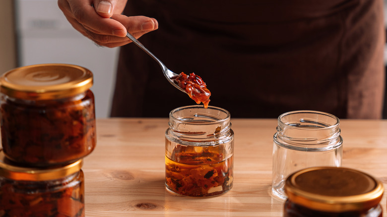 man spooning tomato marinade from jar