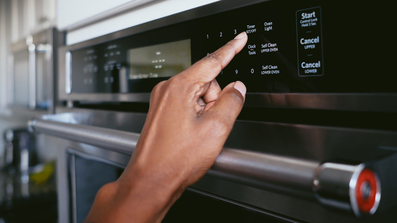 A woman's hand pressing the timer on an oven