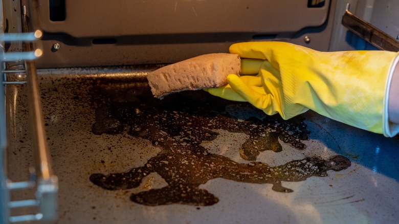 A gloved hand cleaning an oven with a sponge