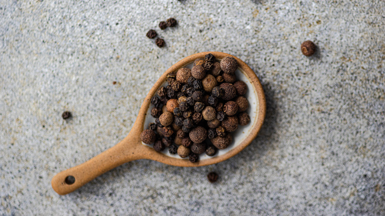 Whole black peppercorns on a wooden spoon