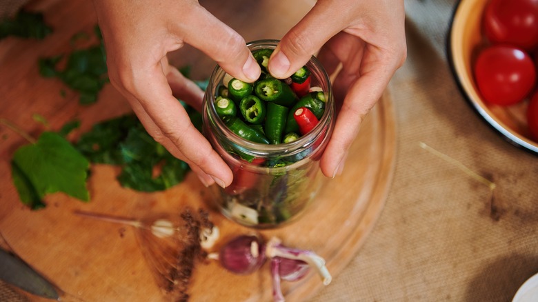 women putting chili peppers into glass jar