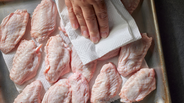 hand pats chicken wings dry with paper towel