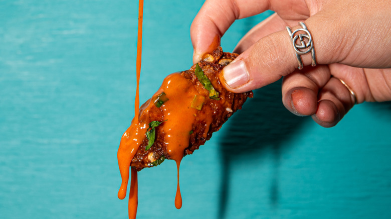 hand holding wing with sauce dripping off