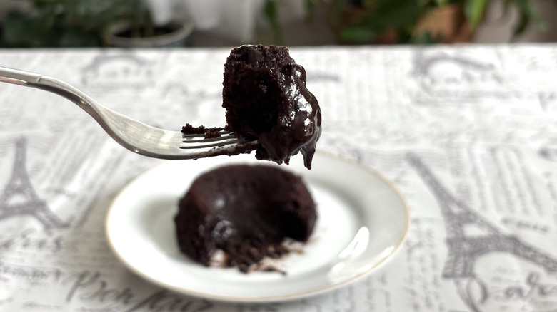 A piece of Trader Joe's Chocolate Lava Cake on a fork with the remaining gooey cake in the background on a plate