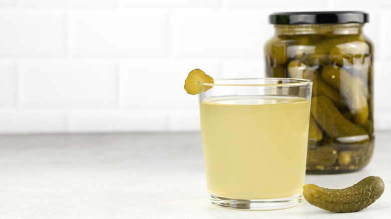 pickle juice in a glass in front of a jar of pickles