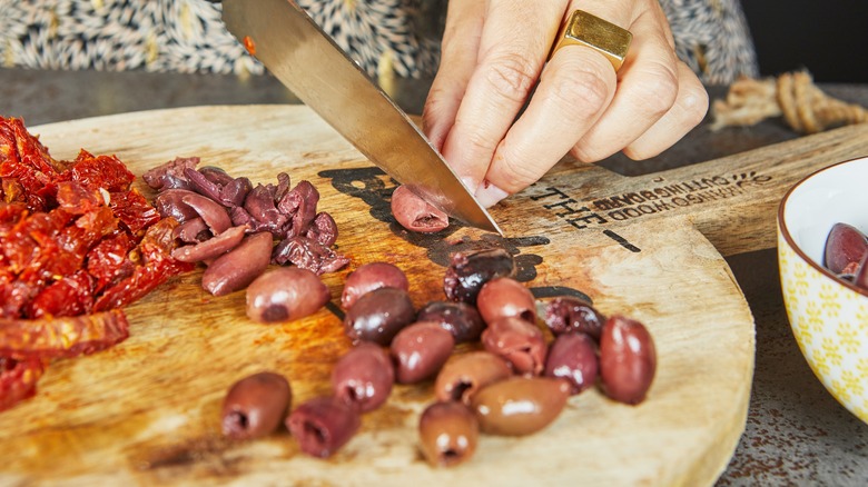 person cutting sun-dried tomatoes and olives