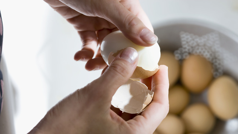 person peeling hard-boiled egg above bowl of eggs