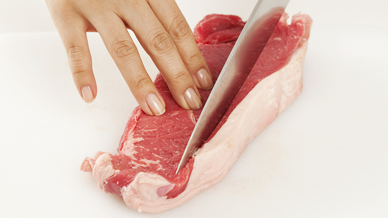 A knife trimming a beef cutlet