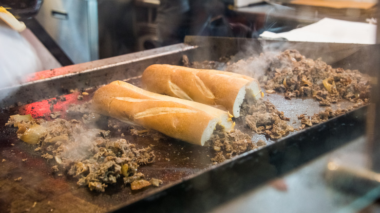 Cheesesteaks and rolls heating on flattop