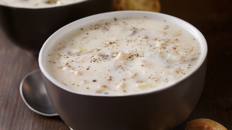 A white and brown bowl of New England clam chowder with pepper cracked on top