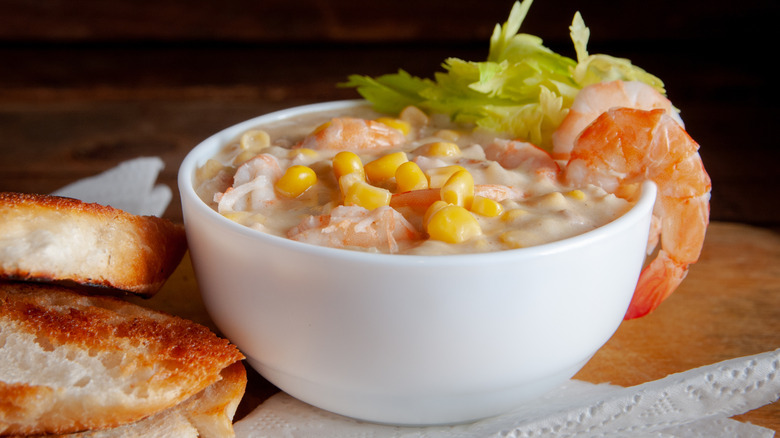 A white bowl of seafood chowder with corn and shrimp with toasted bread