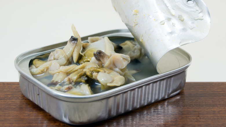 A tin of canned clams in their broth on a wooden table