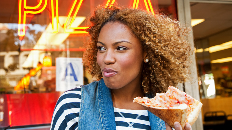 woman holding folded pizza outside of pizzeria