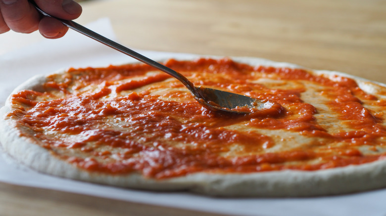 person lightly saucing pizza dough stretched