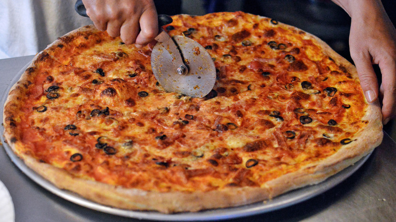 Person cutting large pizza with olives