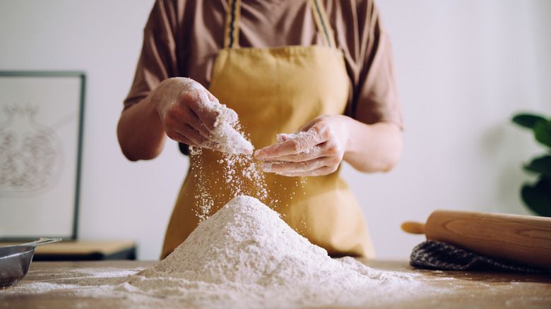 person wearing apron standing in front of pile of flour