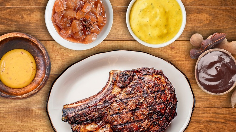 grilled pork chop surrounded by sauces in bowls