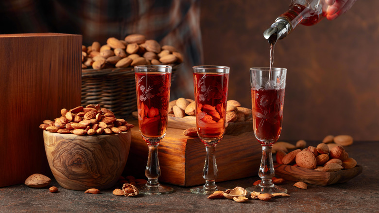 Amaretto liqueur is poured into three glasses set in front of bowls of whole and peeled almonds.