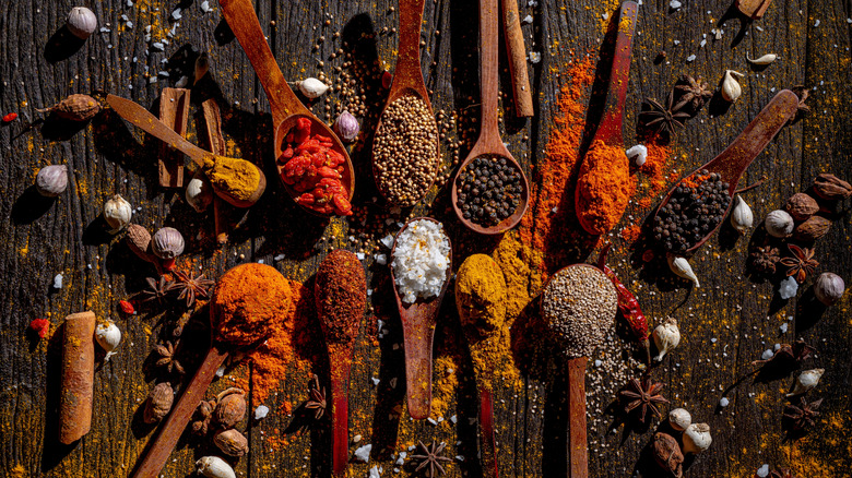 Wooden spoons full of vibrantly colored spices are arranged on a dark wooden table.